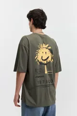 Remera verde militar de algodón, corte oversize, manga corta y cuello redondo. Estampa en la espalda con un círculo amarillo que simula un sol con una cara sonriente, debajo el logo de la marca "Mistral" y el número "1976CO".