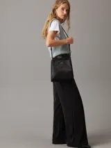 Cartera tipo saco Calvin Klein color negro, con correa ajustable para el hombro, compartimento central con cremallera, compartimento con cierre giratorio en la parte delantera, compartimento magnético en la parte trasera y herrajes plateados con el monograma de la marca.