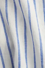 Camisa de corte holgado en tejido liviano de lino y viscosa, con cuello clásico, botones frontales, pliegue en la espalda, hombros caídos, mangas al codo y bajo redondeado. Diseño a rayas verticales azules y blancas.
