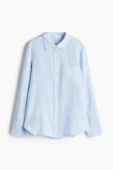 Camisa celeste de lino liviano, con cuello, botones al frente, canesú de doble capa en la espalda, hombros caídos, mangas largas con puños abotonados, bolsillo superior de parche y bajo levemente redondeado.