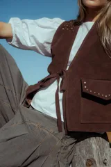 Chaleco marrón de cuero con tachas doradas, forrado y con bolsillos.