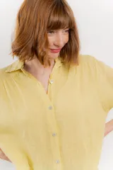 Camisa amarilla de lino con corte recto y calce suelto. Tiene cuello camisero, botones en el frente y mangas cortas con presilla y botón.
