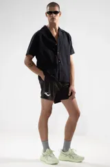 Short de baño negro con cintura elástica y cordón ajustable. Presenta bordados de sirenas en ambas piernas, bolsillos laterales y trasero con cierre. Incluye suspensor de malla fina hipoalergénico.