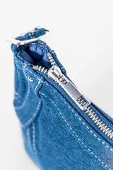 Cartera negra de denim con costuras blancas en contraste, cierre superior con cremallera y asa corta con hebilla ajustable.