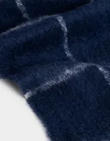 Bufanda tejida azul marino con diseño a cuadros blancos y terminación de flecos trenzados.