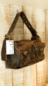 Bolso bandolera color borgoña con textura símil piel de cocodrilo, con correa fina ajustable y dos bolsillos frontales con cierre de broche metálico.