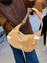 Bolso de corderito beige con múltiples tachas decorativas y cierre metálico.