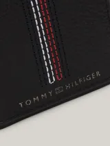 Billetera plegable Tommy Hilfiger de cuero negro con sutil acabado granulado. Presenta costuras distintivas en rojo, blanco y azul en el frente y logo de la marca en la parte inferior.