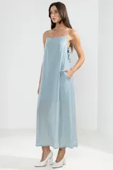 Vestido largo hasta el tobillo color celeste, de tejido arrugado liviano, con escote recto y breteles finos. Presenta lazos en los costados, forro hasta arriba de las rodillas y caída posterior más larga.