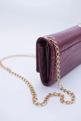 Cartera tipo sobre color beige con textura granulada y correa de cadena dorada.