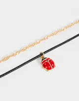 Set de dos chokers: uno de cadena dorada y otro de cordón negro con dije esmaltado de vaquita de San Antonio.