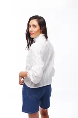 Camisa blanca de algodón con cuello alto con volados, mangas largas abullonadas y cierre frontal con botones.