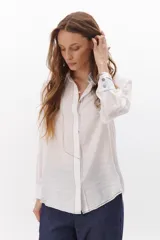 Camisa negra de manga larga con cuello clásico y cierre frontal con botones. Presenta costuras decorativas en color blanco.