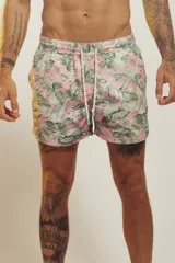 Short de baño para hombre, tiro medio, con estampado tropical en tonos rosados, verdes y blancos. Posee cintura elástica con cordón de ajuste trenzado y bolsillos laterales.
