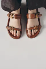 Sandalias planas negras con dos tiras anchas y hebillas doradas.