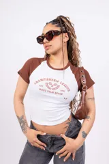 Remera corta blanca con mangas raglán negras, cuello redondo y estampado frontal con el texto "Championship League Est. 1996 West Palm Beach" y dos raquetas de tenis cruzadas.