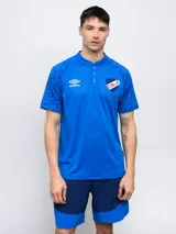 Remera polo de entrenamiento del Club Nacional de Football, color azul con diseño geométrico en mangas y hombros, logo de Umbro bordado en el pecho y escudo del club. Cierre con botones en el cuello.