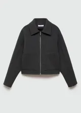Chaqueta negra corta con capucha gris desmontable y ajustable con cordones. Presenta cuello camisero, cierre de cremallera doble, bolsillos laterales y bajo con goma elástica.