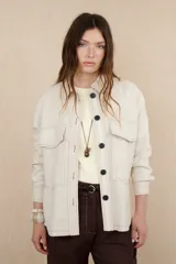 Sobrecamisa color beige de lino con cuello camisero, cierre frontal con botones negros, mangas largas con puños abotonados, dos bolsillos de parche en el pecho y dos bolsillos laterales.