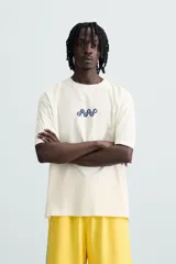 Camiseta blanca de corte holgado, cuello redondo y manga corta. Estampado frontal y trasero con gráficos y textos combinados en color azul.