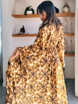 Kimono largo de seda con estampado floral en tonos verde, marrón y beige. Tiene mangas amplias y corte cruzado con lazo ajustable en la cintura.