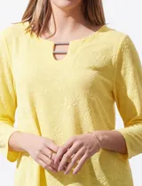 Blusa blanca de tejido labrado con cuello redondo, escote en V y aplique metálico.