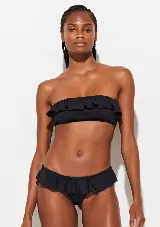 Conjunto de bikini negro con corpiño con escote recto y volados en los breteles y contorno superior, y bombacha clásica con volados en la cintura.