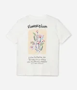 Remera de algodón color crudo, de corte alargado, con cuello redondo, mangas cortas y estampa floral con lettering Flowers Bloom en el frente.