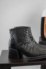 Botines negros de cuero con textura tipo cocodrilo, cierre trasero con cremallera y tacón geométrico.