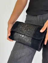 Cartera de mano tipo sobre, color negro con textura símil piel de cocodrilo.