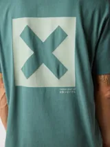 Camiseta de manga corta color azul grisáceo, con un gran estampado cuadrado turquesa en la espalda que contiene una 'X' blanca. Pequeño logo bordado en la parte superior de la espalda.