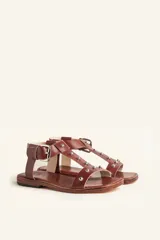 Sandalia de cuero color marrón con tiras finas, detalles de tachas metálicas y hebilla lateral.