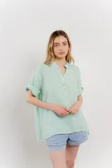 Blusa blanca de lino con escote en V abotonado y mangas cortas arremangadas.
