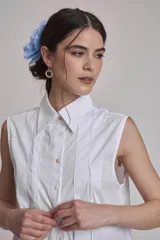 Camisa azul marino sin mangas con cuello clásico, abotonada al frente y detalle de plisados verticales en el pecho.