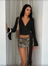 Top blanco de encaje con escote en V, mangas largas acampanadas y lazo lateral para ajustar.