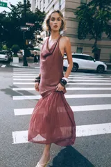 Vestido midi color lila, de cuello halter y sin mangas. La parte superior es de tejido arrugado y la falda es plisada. Tiene abertura en la espalda con cierre de botones ocultos.