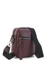 Bandolera de cuero sintético en color marrón claro con apertura superior de cierre. Presenta un bolsillo frontal con cierre y una correa de galón ajustable y desmontable con diseño a rayas. El interior incluye un bolsillo de fácil acceso.