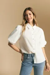 Camisa blanca de manga corta con volumen en los hombros, cuello camisero y cierre frontal con botones dorados.