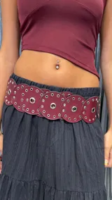 Cinturón ancho de cuero sintético color bordó, con apliques circulares grandes y pequeños remaches metálicos.