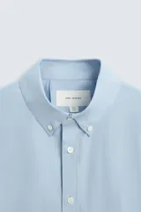 Camisa celeste de corte regular fit, confeccionada en popelín de algodón. Tiene cuello abotonado, manga larga con puños abotonados y cierre frontal con botones.