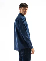 Camisa de manga larga color verde oliva, confeccionada en algodón. Tiene corte clásico, bolsillo en el lado izquierdo del pecho y cierre con botones.