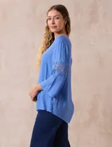 Blusa celeste de gasa bambula con cuello a la base y escote en V. Manga ¾ amplia, con aplique de crochet en los puños.