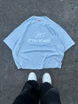 Remera celeste de corte holgado con cuello redondo y estampado en relieve con el logo de la marca y la frase "Ittai Stars".