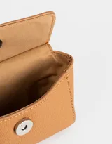 Monedero de cuerina color crudo con estampado de motivos japoneses y la palabra "Tokyo". Tiene forma de bolso con manija superior, solapa con broche a presión y mosquetón lateral.