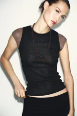 Top de manga caída, con efecto de doble capa. La capa exterior es negra y ajustada, mientras que la capa interior, visible en mangas y cuello, es de color marrón topo.