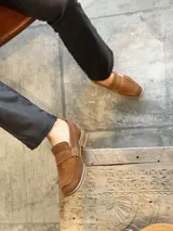 Mocasín de gamuza color marrón claro con detalle de hebilla y suela clara.