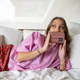 Billetera corta con cierre alrededor y tapa, confeccionada en tela capitoneada. Incluye varias reparticiones con tarjeteros y bolsillos internos, y una correa de mano desmontable. Disponible en negro, rojo y dorado.