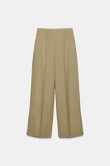 Pantalón ancho de tiro medio, color verde oliva, confeccionado en lino 100%. Presenta pliegues marcados en la parte delantera y bolsillos laterales ocultos.