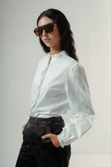 Camisa blanca de manga larga con cuello mao y volados verticales en la botonera frontal.