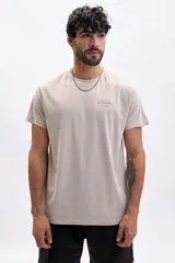 Remera de manga corta color taupe, con cuello redondo y estampado minimalista en el pecho que indica "EST. 1975 ST. ÉTIENNE FRANCE".